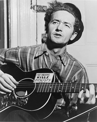 Woody Guthrie, wielding the Guitar of Fascists' Bane